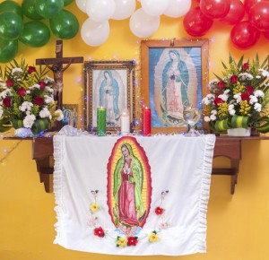 Altar to Our Lady of Guadalupe with framed pictures, flowers, candles, cross