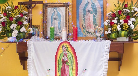 Altar to Our Lady of Guadalupe with framed pictures, flowers, candles, cross