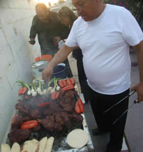 Man cooking carne asada, peppers, onions, and tortillas on an open grill in Mexico