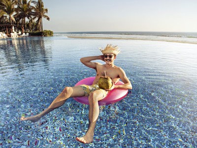 Man lounging in a pink float in the water with coconut drink