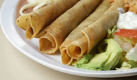 Flautas sitting on a white plate with avocado