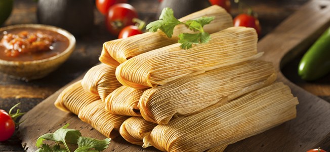 9 tamales stacked on a wood cutting board