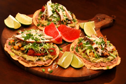 3 tostadas sitting on a round wood cutting board with lime and grapefruit