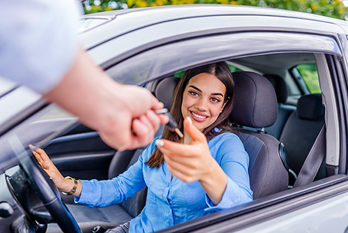 Woman in driver's seat of car being handed the key to rental car through window