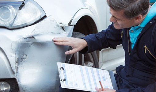 Insurance adjuster touching and looking at damage to vehicle front side panel