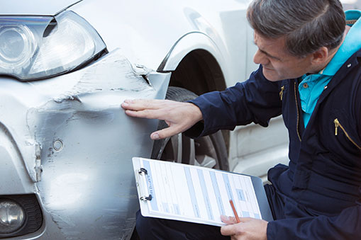 Insurance adjuster touching and looking at damage to vehicle front side panel