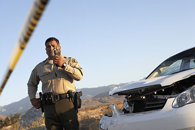 Police Officer using walkie talking at the scene of an accident in Mexico, damage to car front grill shown